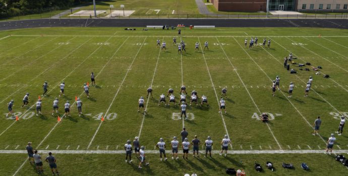 "Aerial view of a football practice field with players spread across drill stations"