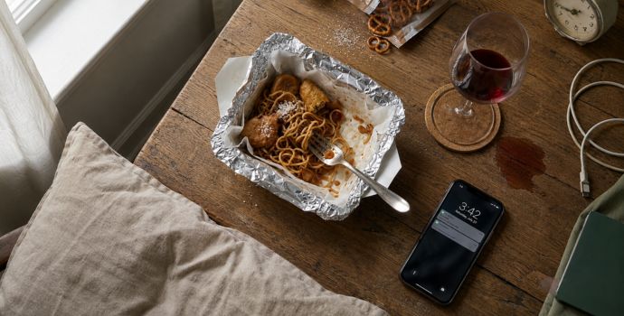 Flat-lay of everyday causes of facial puffiness including salty food, wine, a late-night phone, and a pillow"